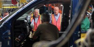 Two employees watching as an automobile is assembled on the GM assembly line